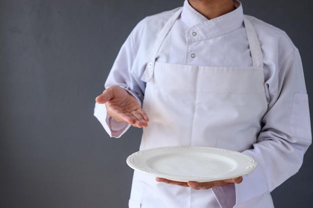 Cropped image of a male chef in white apron holding an empty plate with arm presenting gesture.