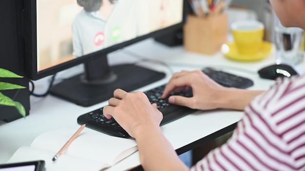 Cropped image of man is typing on a keyboard while making a video conference at the working desk.