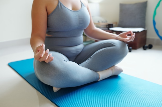 Cropped image of plus size woman sitting In lotus position on yoga mat, mindfulness and spirituality concept