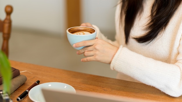 Cropped image of Relaxed female in comfy white sweater drink sip hold hot cappuccino coffee cup