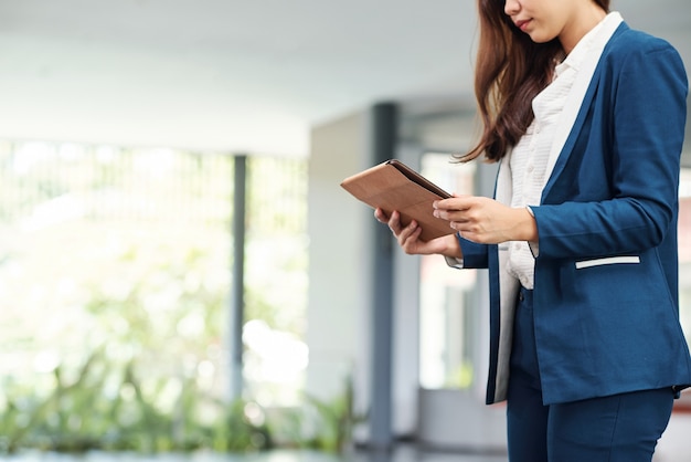 Cropped image of serious young businesswoman reading article on tablet computer