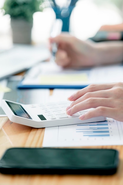 Cropped image of woman hand using calculator, working with graph chart and analyzing business strategy, financial statistic, siiting at desk office, veritcal view.