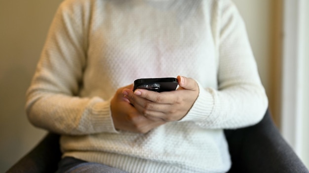 Cropped image of a woman using her phone while sitting at a chair in a coffee shop