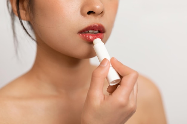 Cropped of korean lady using lipbalm taking care of her beautiful lips putting hygienic lipstick