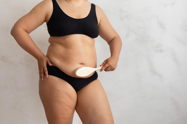 Cropped overweight adipose female rubbing stomach e skin using stiff exfoliating brush cellulite dry lymph massage