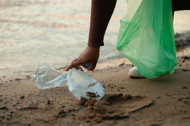 Cropped photo of African woman picking up spilled trash from sand on beach in green plastic bag Ecology pollution