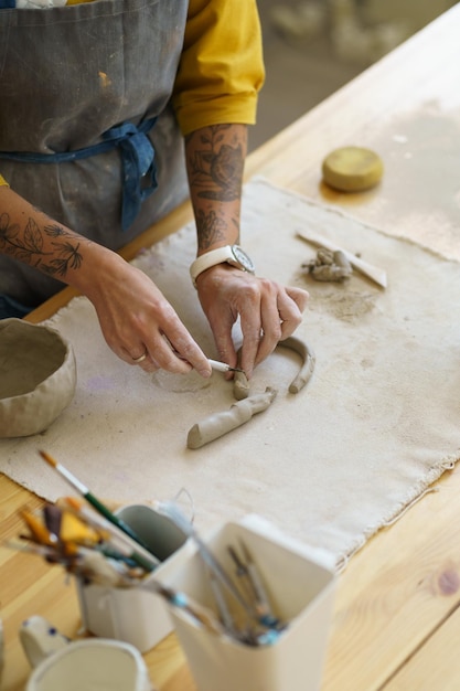 Cropped photo of artisian craftswoman potter standing by table in studio and making clay pottery