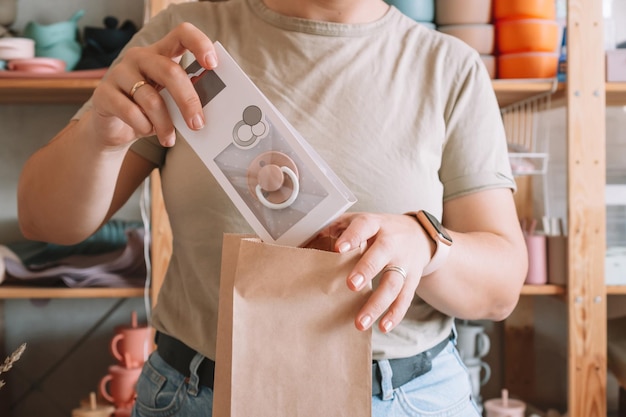 Cropped photo of businesswoman hands packing preparing parcel Woman puts pacifier in kraft paper bag Close up