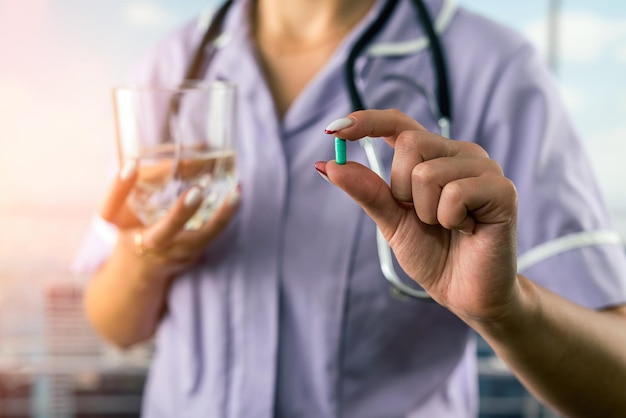 Cropped photo of female doctor holding pill and glass of water in two hands in hospital