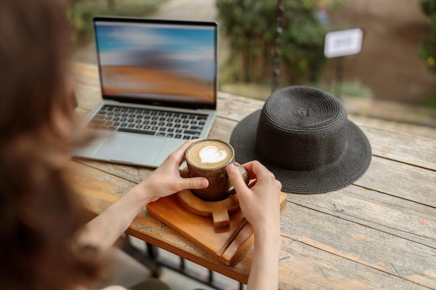 Photo cropped photo of lady holding cup of coffee while working with laptop outdoors in cafe