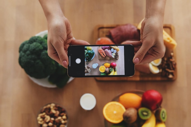 Cropped photo of a person holding smartphone and taking picture of an array of different food products on the table