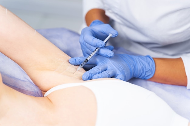 Cropped photo of a young lady receiving injection into the armpit in a clinic