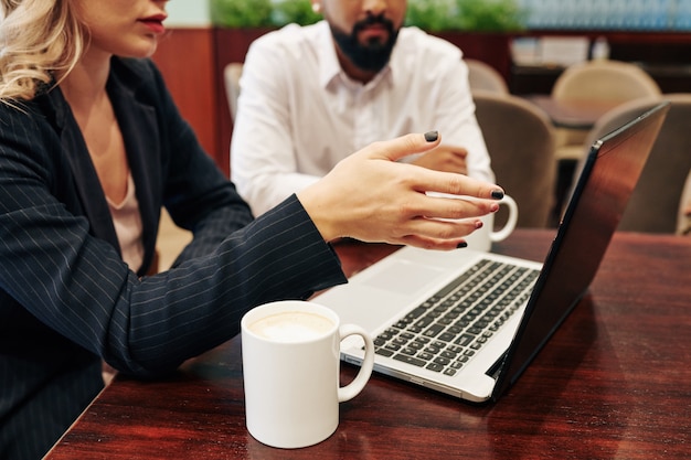 Cropped portrait of business people drinking coffee and watching presentation on laptop