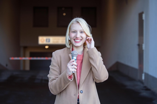 Cropped portrait of professional female reporter at work Young woman standing on the street with a microphone in hand and smiling at camera Horizontal shot Selective focus on woman