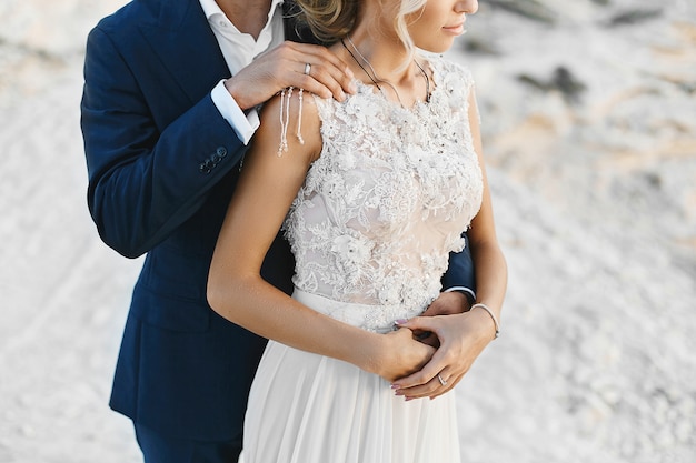 Cropped portrait of a young fashionable couple, handsome man hugs a sexy young woman in a lace dress. Young businessman posing with a beautiful model girl on a seacoast