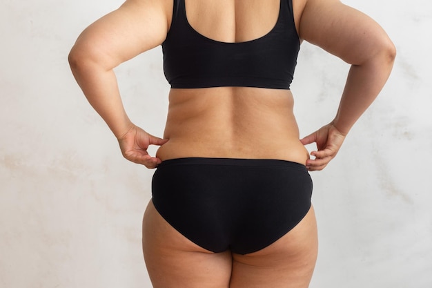 Cropped rearview of overweight female body in black lingerie checking and holding excess fat back folds Health dieting