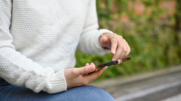 Cropped short of hand holding smartphone female using smartphone in the park