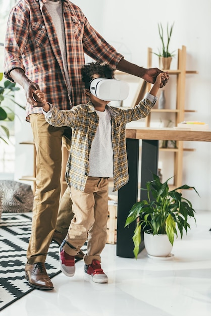 Cropped shot of africanamerican father and son in vr headset holding hands in office