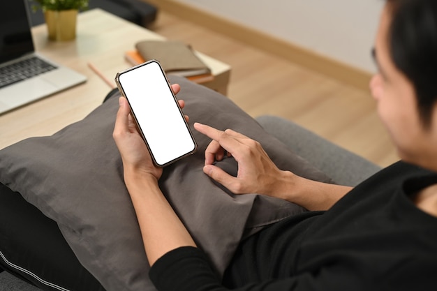 Cropped shot Asian man resting on sofa and using mobile phone.