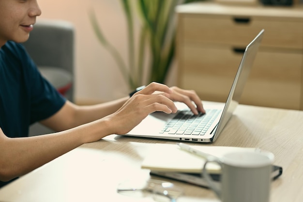 Cropped shot of asian man sitting in cozy living room and surfing internet with laptop computer