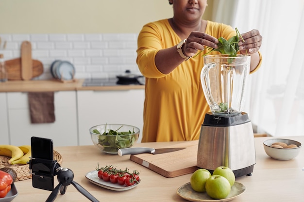 Cropped shot of black woman putting spinach in blender while making healthy smoothie at home copy sp