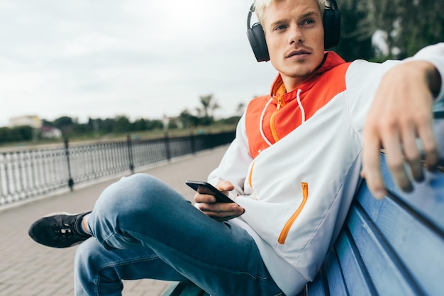 Cropped shot of blond young man enjoying and listening music from his smart phone on bluetooth headphones outdoor in the park xA Lifestyle technology and people concept