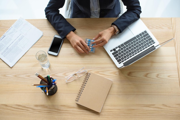 Cropped shot of businesswoman holding vitamins in hands at workplace with digital devices and