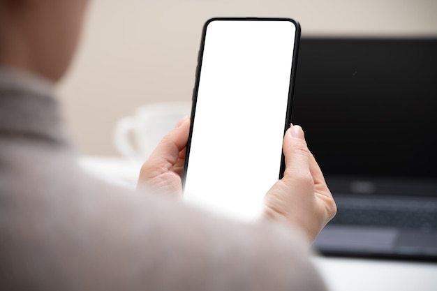 Cropped shot of businesswoman looking at blank screen smartphone in modern office room woman hand holding phone with white screen in office woman using cell phone at workplace