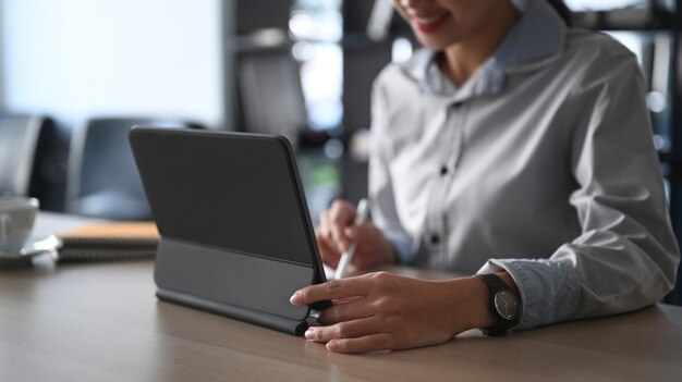 Cropped shot of businesswoman searching information on computer tablet at office desk.