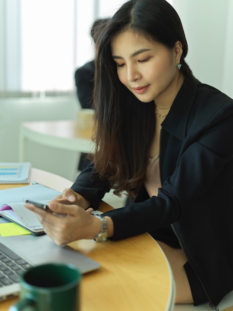 Cropped shot of businesswoman using smartphone while sitting at workplace