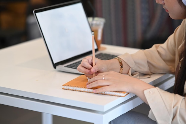 Cropped shot of businesswoman writing something on notebook and working with computer laptop at office desk.