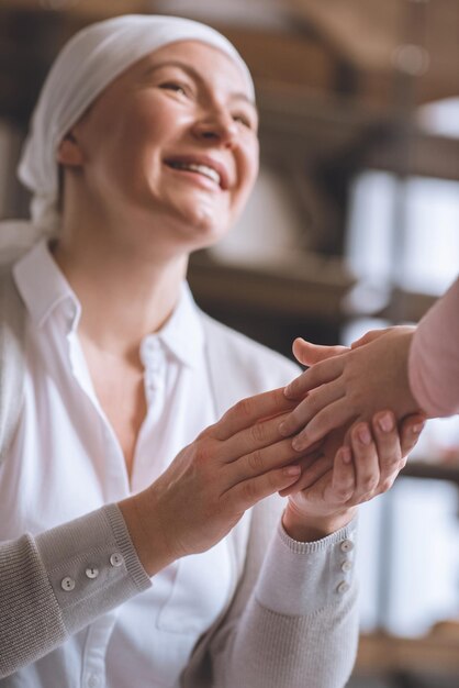 Photo cropped shot of child and smiling sick mature woman in kerchief holding hands