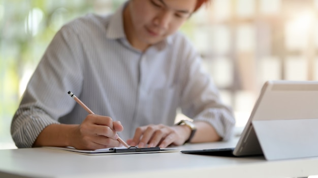 Cropped shot of entrepreneur writing an idea on notebook while working with digital tablet