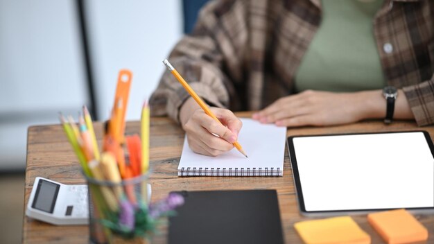 Cropped shot female accountant working with digital tablet and making notes on notebook