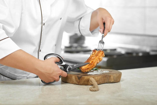 Cropped shot of a female chef preparing delicious grilled chicken steak at her kitchen cutting it with scissors copyspace restaurant food eating meat concept.