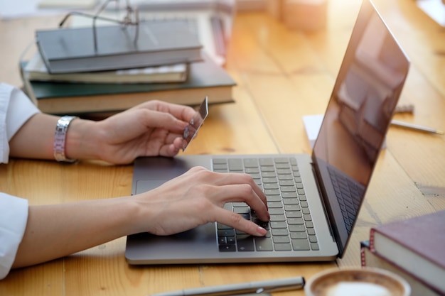 Cropped shot of female hand holding plastic credit card and using laptop. Online shopping payment concept.