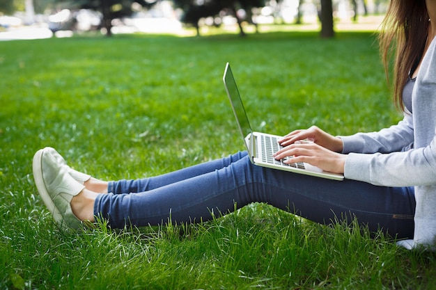 Cropped shot of freelancer girl with laptop outdoors. Young woman working on pc at city park. Technology, education and remote working concept