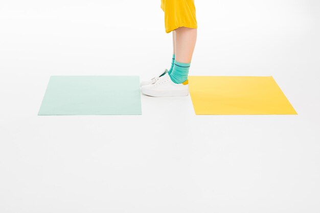 Cropped shot of girl dressed in yellow with turqouise socks isolated on white with colored papers