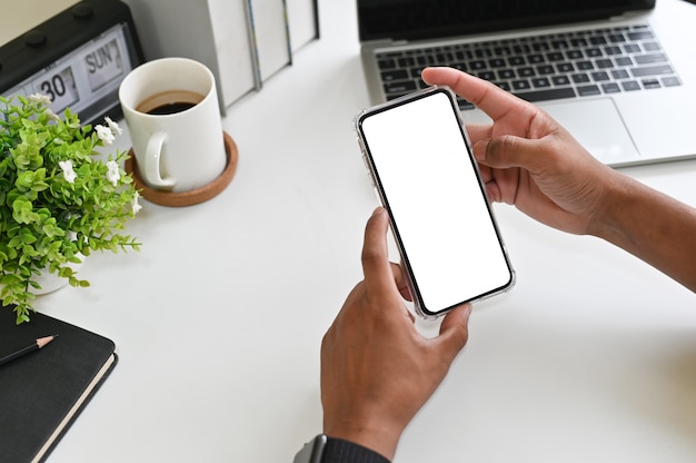 Cropped shot hands using mockup smartphone on office desk with clipping path.