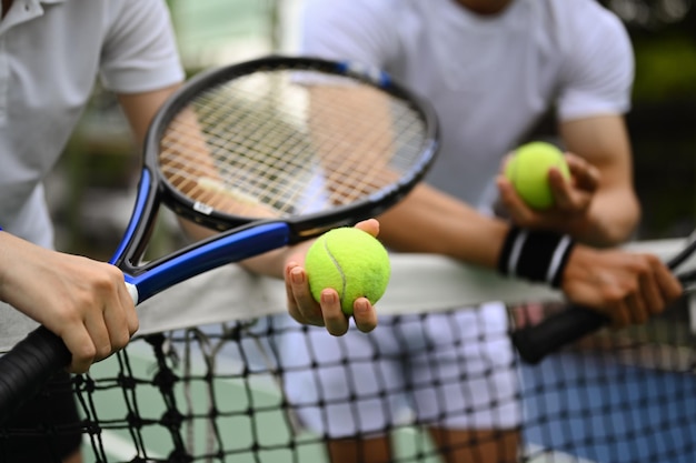 Cropped shot of male tennis coach giving instructions to his student standing by net at the outdoor tennis court