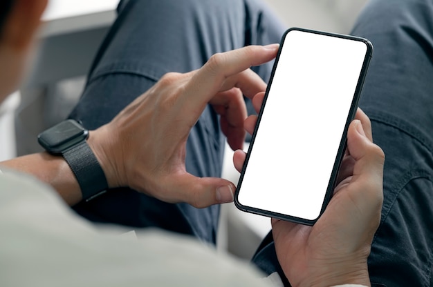 Cropped shot of man hands using smartphone with blank screen while sitting in living room at home.