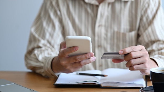 Cropped shot man holding smart phone and credit card for payment online.