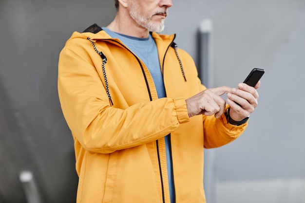 Cropped shot of senior man using smartphone outdoors against concrete background copy space