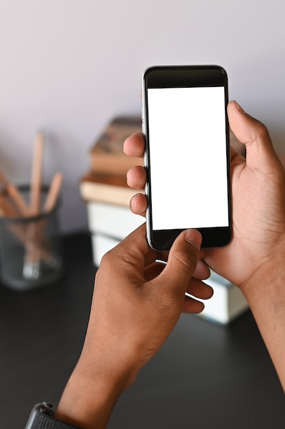 Cropped shot of smartphone on hands with empty screen on office desk.