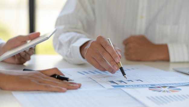 Cropped shot of A team of employees points the graph and uses a tablet for the data.