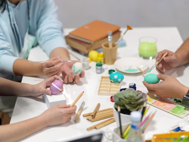 Cropped shot of teenagers hands painting easter eggs, preparing for easter festival with painting tools