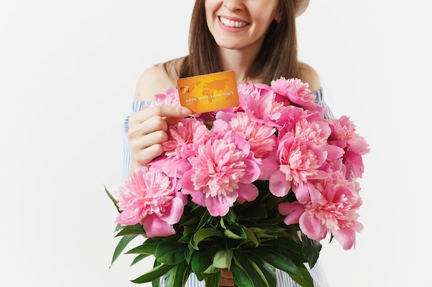 Cropped shot woman in blue dress, hat holding credit bank card, money, bouquet of beautiful pink peonies flowers isolated on white background. Business, delivery, online shopping concept. Copy space.