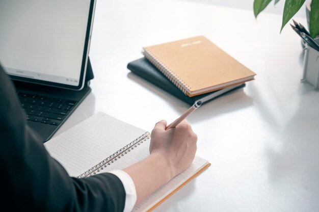 Cropped shot of woman hand writing on notebook while sitting at her office desk.