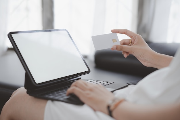 Cropped shot of woman hands using tablet white screen computer shopping online with mockup credit card at home.