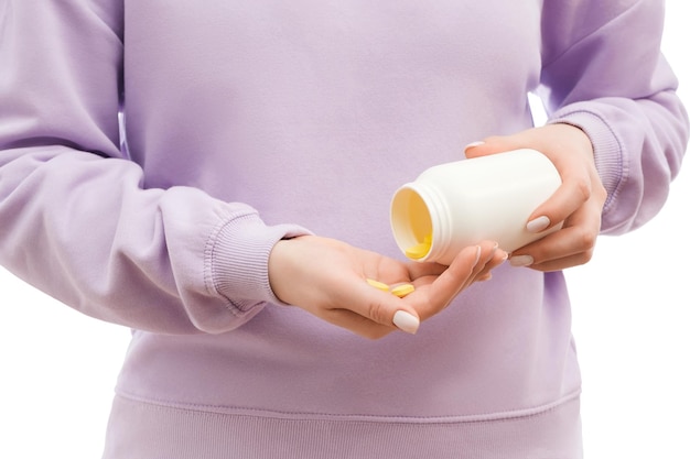 Cropped shot of a woman in a lavander oversized sweatshirt pours out yellow pills of the big white bottle